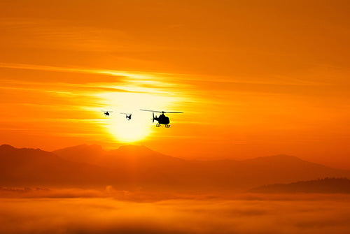 Helicopter flying against a bright orange sunset with mountains in the background
